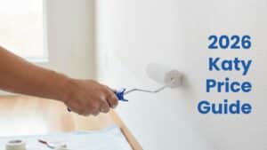 A professional painter using a roller to apply beige paint to a high interior wall, part of a guide on the cost of painting services.